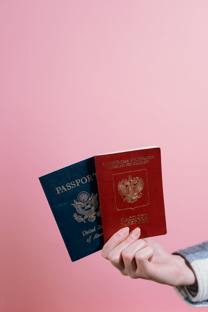 services-03 Close-up of two passports held by a hand against a pink background.